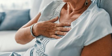 Woman sat on sofa holding her hand over her chest