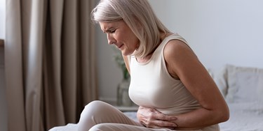 Woman holding her stomach due to acute abdominal pain on bed